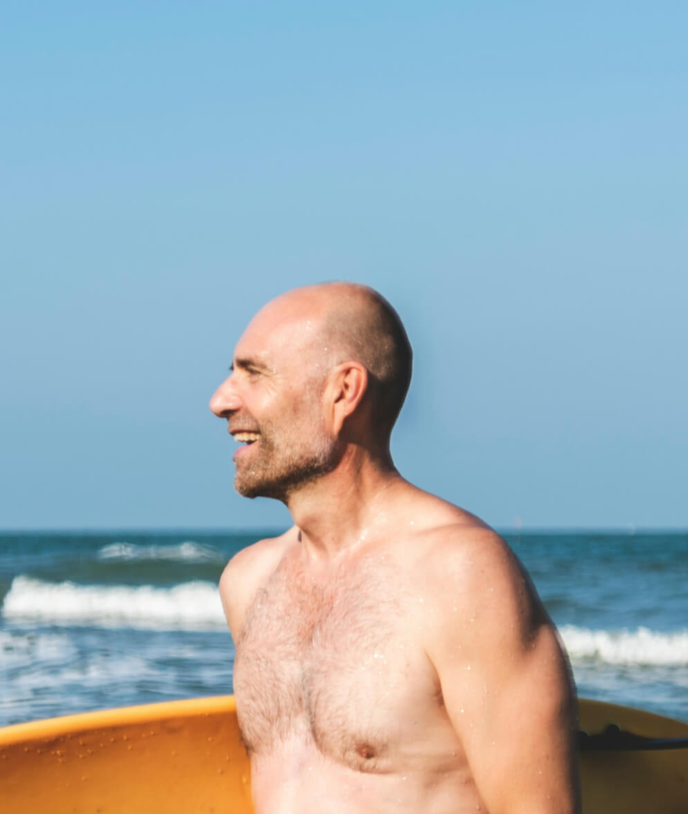 A man holding a surfboard while smiling at the beach